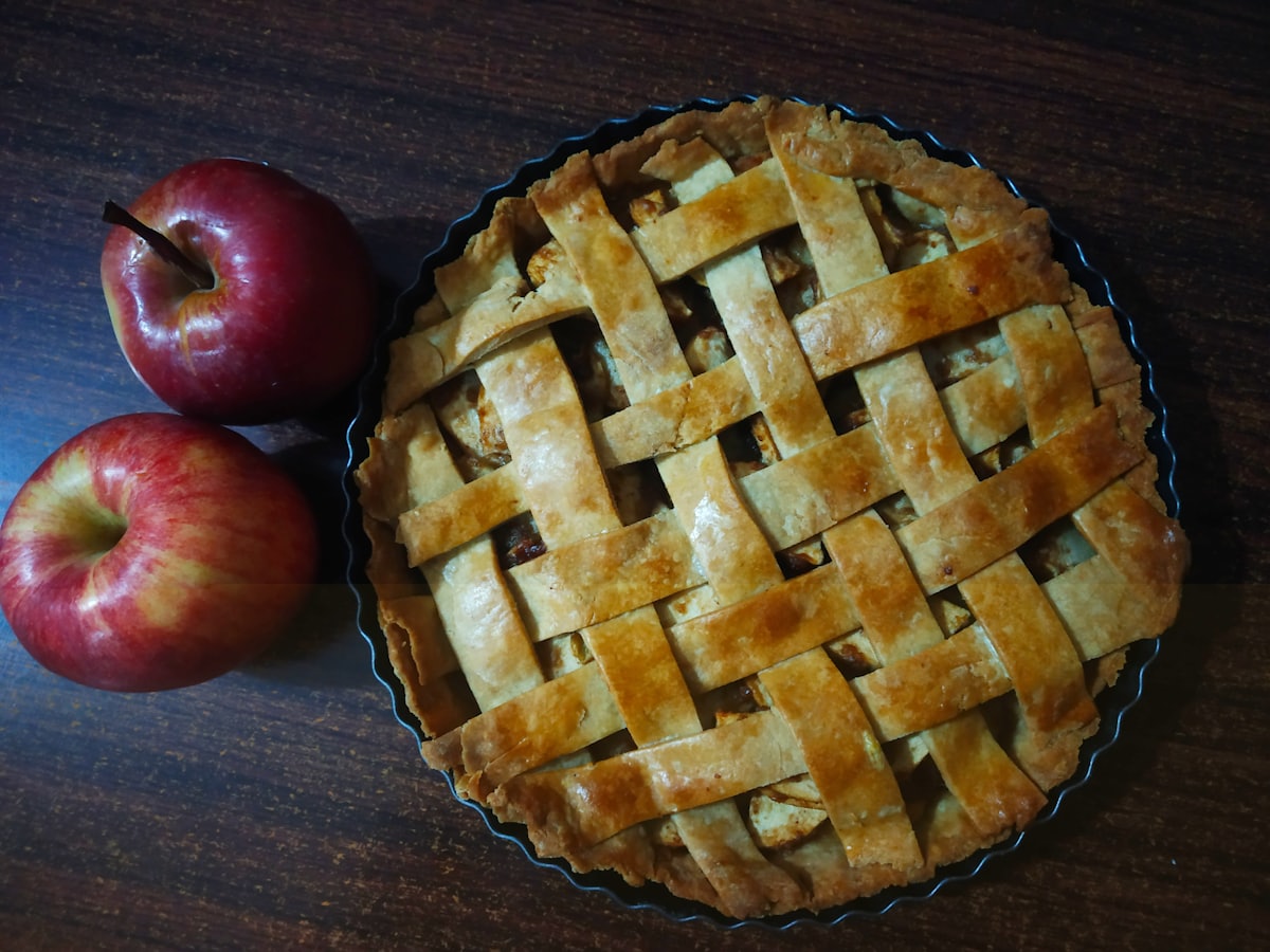 A golden apple strudel beside two fresh red apples