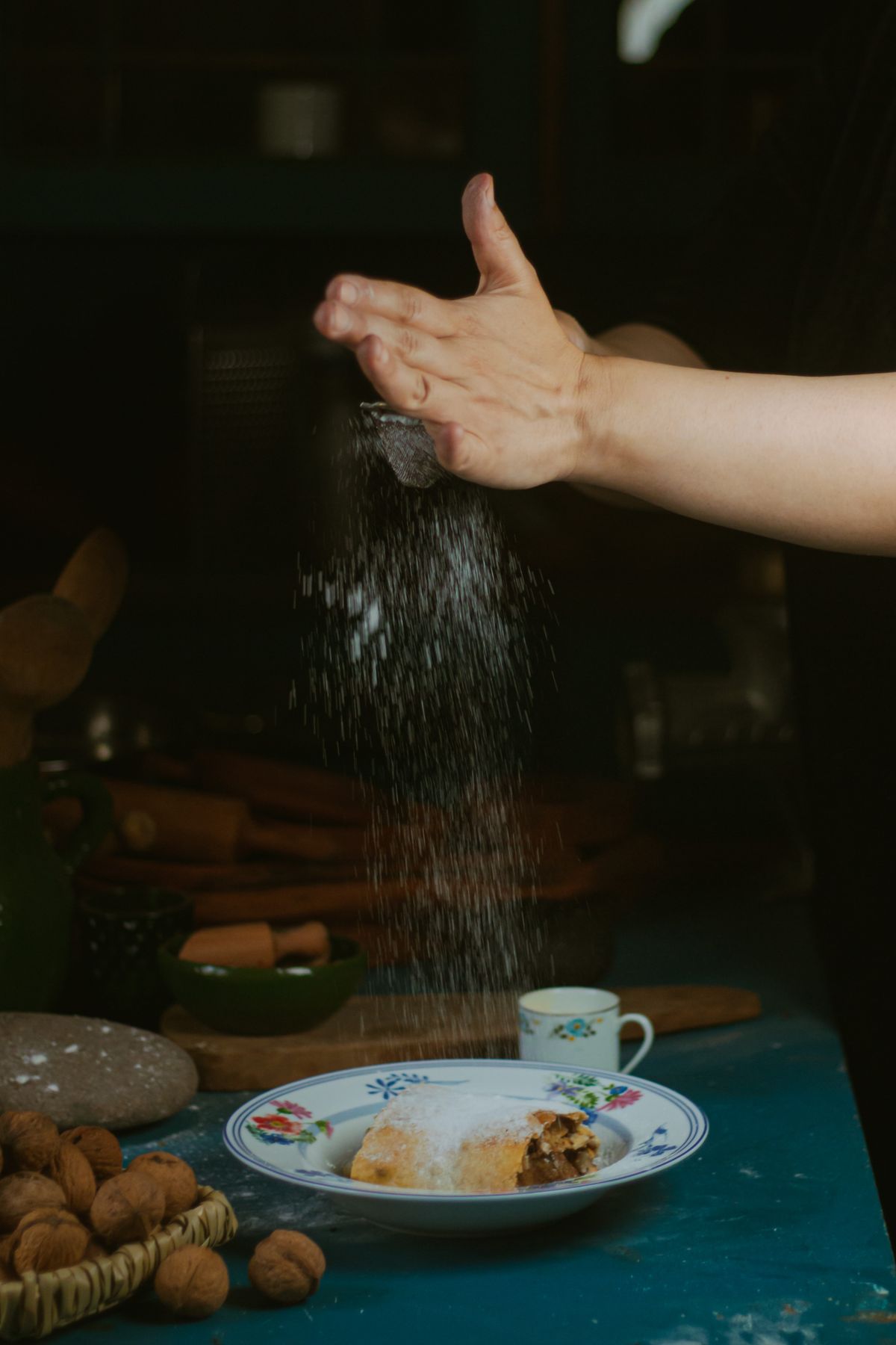 Icing sugar being dusted by hand over a slice of apple strudel