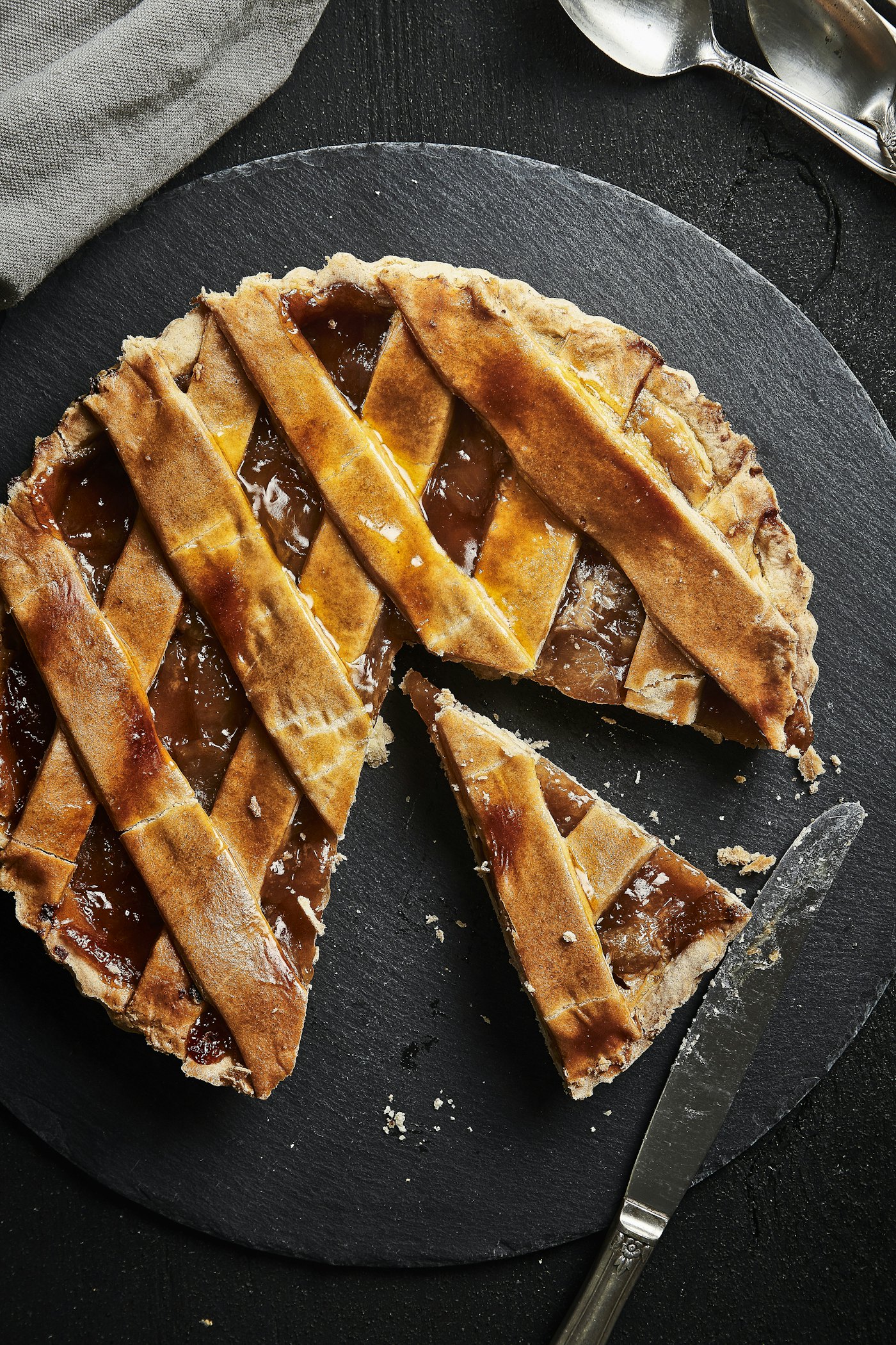 A lattice-topped apple strudel on dark slate with one slice cut