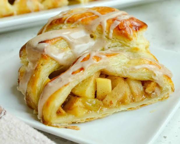 A whole apple strudel in flaky puff pastry with icing drizzled over the top